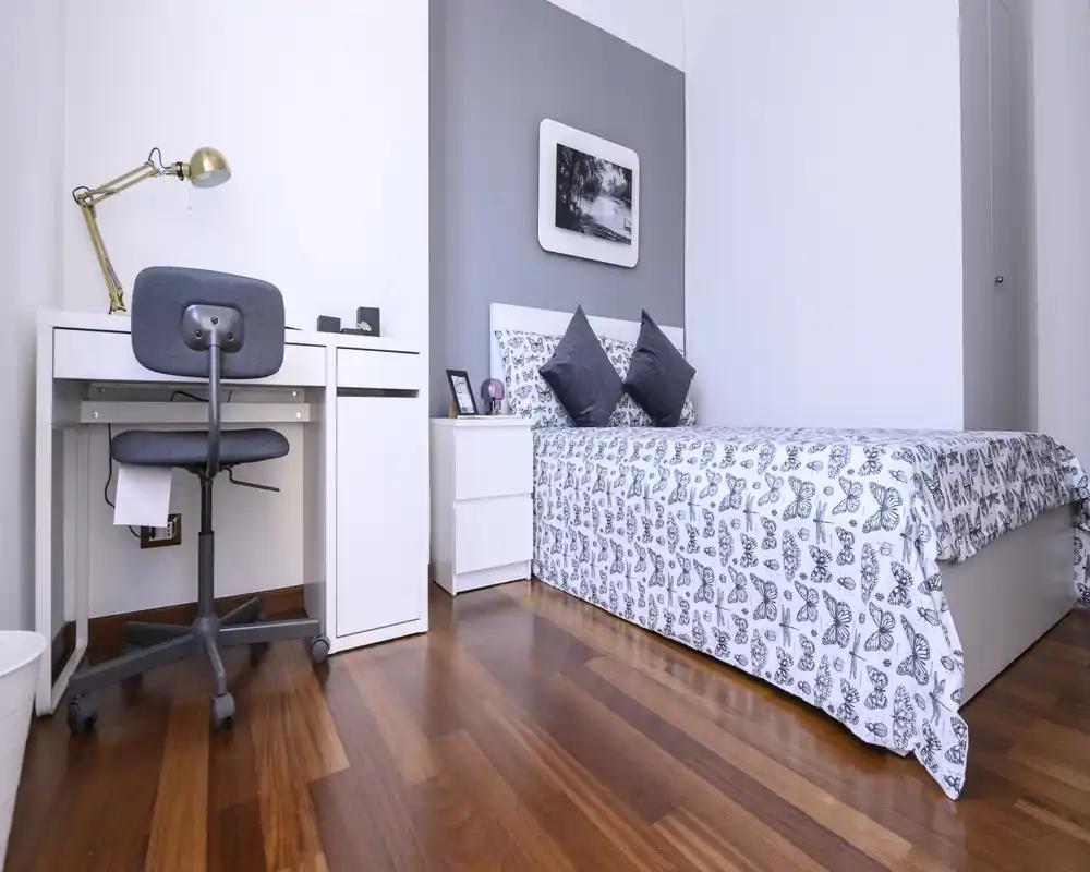 Bright, neatly staged bedroom with a patterned duvet, two decorative cushions and a compact desk area — ideal for a single occupant or student.