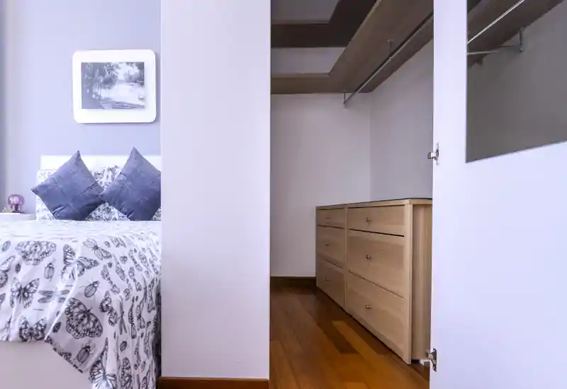 Coin chambre lumineux et soigné avec couette à motifs, coussins décoratifs et placard intégré visible par la porte — parfait pour des photos de location mettant en avant le rangement et le confort.