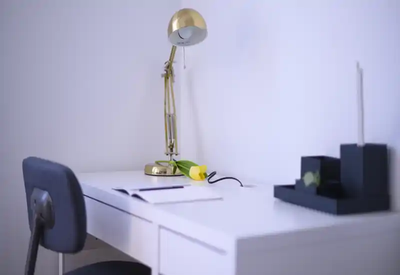 Coin bureau lumineux et minimaliste avec une lampe dorée réglable, une tulipe jaune et une chaise — un petit espace de travail à la maison soigné.