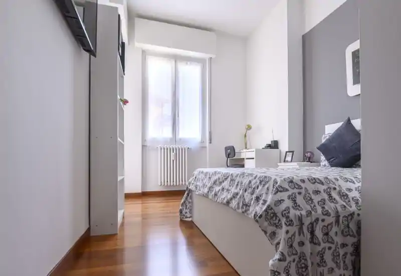 Chambre simple lumineuse et moderne avec couette à motifs, bureau près de la fenêtre et parquet chaleureux — bien éclairée et soigneusement décorée pour les annonces.