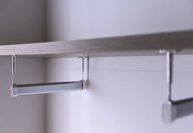 Gros plan d’une tringle de penderie et d’une équerre d’étagère dans une armoire/placard ; contexte de la pièce minimal.