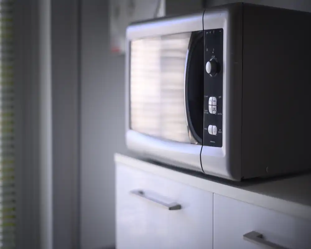 Close-up of a stainless-steel microwave on a white kitchen cabinet, softly lit from the side with a shallow depth of field.