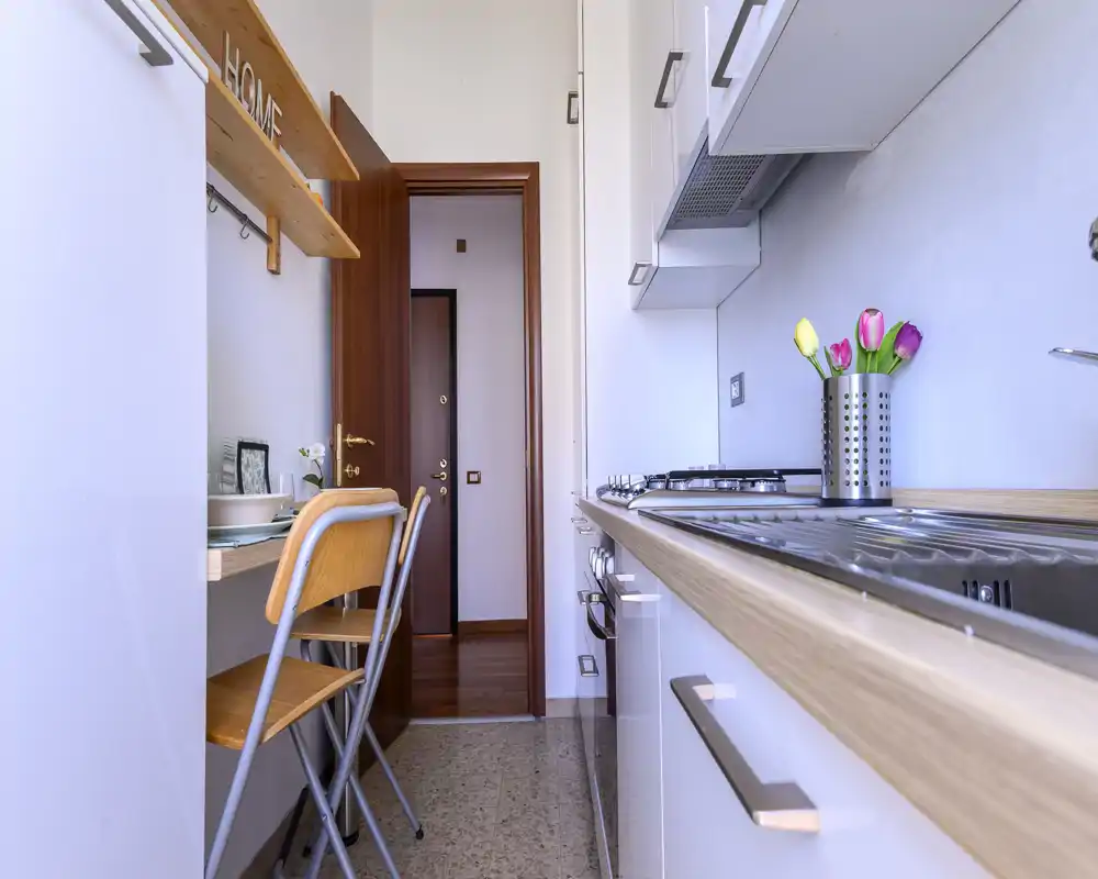 Bright, modern galley kitchen with a wooden countertop, built-in gas hob and a compact breakfast bar with chairs; decorative tulips add a cozy touch.