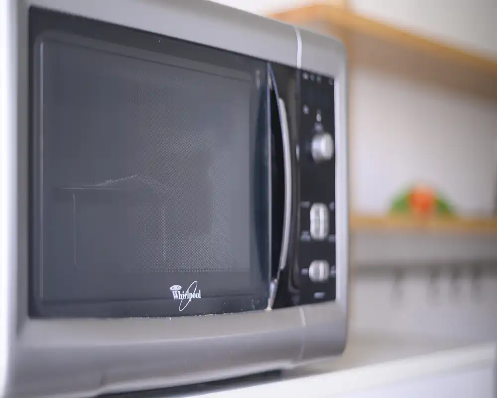 Close-up of a stainless-steel microwave in a bright kitchen; sharp foreground detail with a softly blurred shelf in the background.