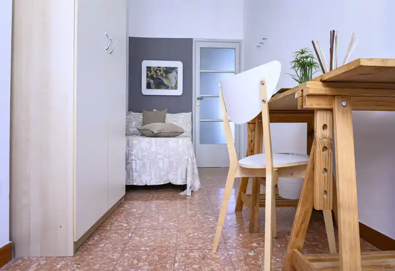 Chambre lumineuse et fonctionnelle avec un lit simple bien fait, une armoire encastrée et un bureau en bois ; lignes épurées et accents boisés pour un espace chaleureux et pratique.