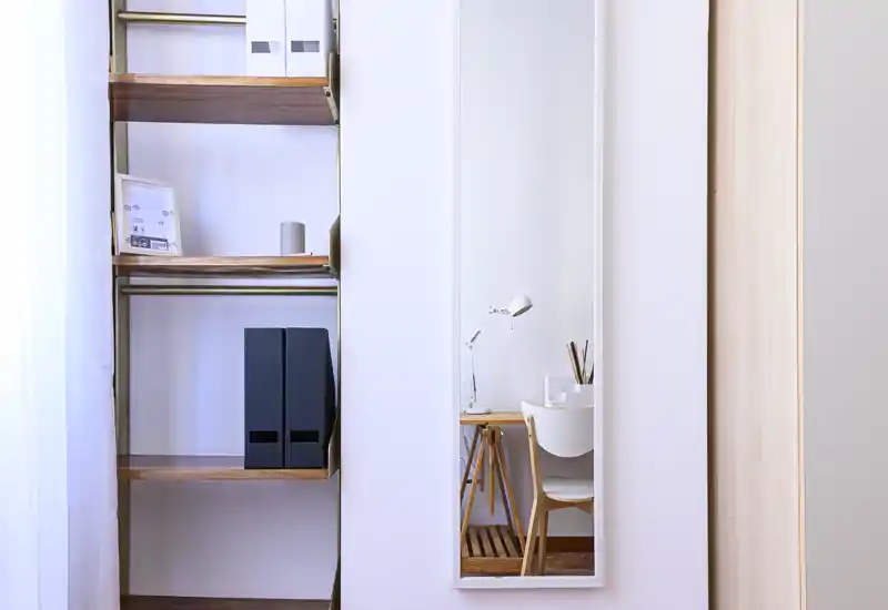 Angolo luminoso e minimal del soggiorno con scaffali e una piccola scrivania visibile nello specchio a parete; linee pulite e luce naturale creano un’area di lavoro tranquilla.