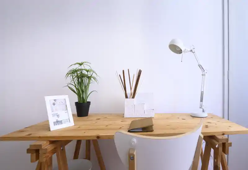 Spazio di lavoro luminoso e minimale in un ambiente living con scrivania in legno, lampada da tavolo, piccola pianta e cornice: ordinato e moderno, ideale per il lavoro da remoto.