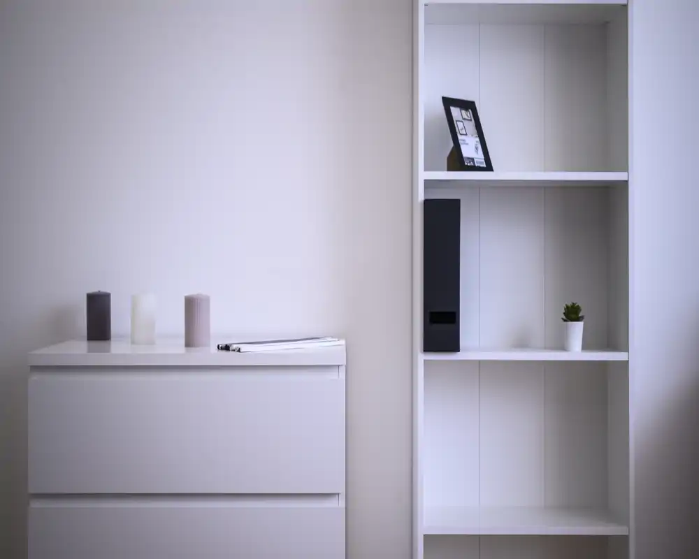 Coin de chambre minimaliste avec une commode blanche et des étagères ouvertes, décoré de bougies, d'une petite plante et d'une photo encadrée — look simple et moderne.