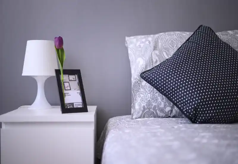 Well-styled bedroom corner with patterned bedding, a decorative polka-dot cushion and a bedside table with lamp and single tulip — bright, calm and inviting.