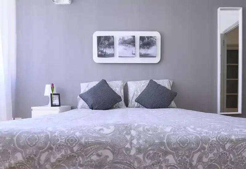 Chambre moderne et lumineuse avec literie à motifs, deux coussins décoratifs et une table de chevet minimaliste ; lumière naturelle douce et tons neutres pour une ambiance apaisante.