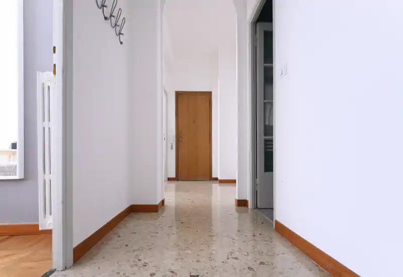 Ingresso luminoso e pulito con pavimento in graniglia, pareti bianche e porta d'ingresso in legno sullo sfondo — ambiente d'ingresso essenziale e ben illuminato.