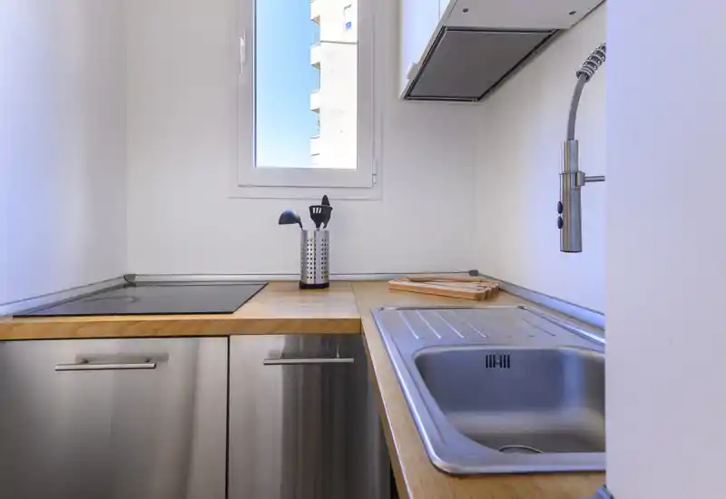 Cucina compatta e moderna con elettrodomestici in acciaio inox, piano in legno e finestra luminosa che offre luce naturale. Zona lavello funzionale e piano cottura a induzione in un layout pulito e minimalista.