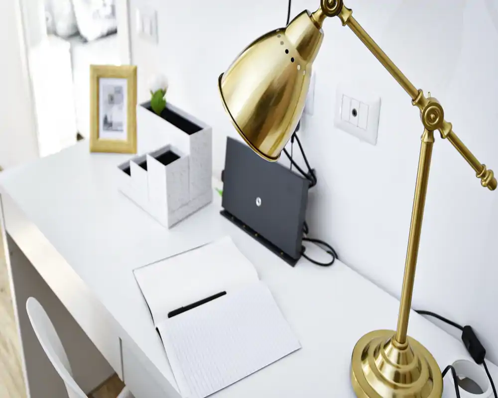 Rincón de escritorio luminoso y moderno con lámpara dorada, cuaderno y organizador—ideal como espacio de trabajo o estudio en el salón.