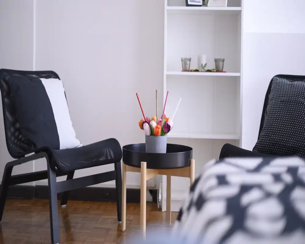 Zona giorno moderna con due poltrone nere, un piccolo tavolino rotondo e fiori decorativi — luminosa, minimal e accogliente.