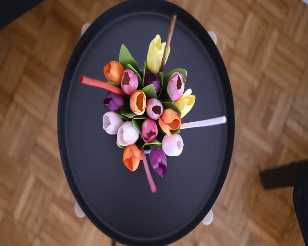 Scatto dall'alto di un piccolo tavolino rotondo con un colorato mazzo di tulipani come dettaglio decorativo; ideale per mostrare lo styling della zona giorno o del tavolo.