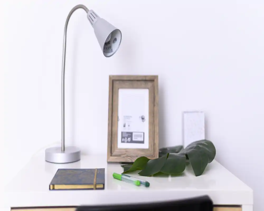 Bright, minimal bedside/desk setup with a modern desk lamp, framed photo, notebook and pens on a clean white surface — suitable detail for a bedroom listing focusing on bedside styling.