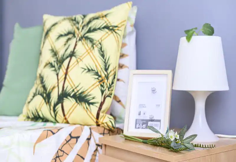 Bright, styled bedroom corner with patterned cushions, a bedside lamp and wooden nightstand, ideal for a cozy rental listing.