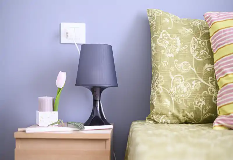 Close-up of a bedroom bedside area with patterned pillows, a bedside table, lamp and decorative details — bright, tidy and inviting.
