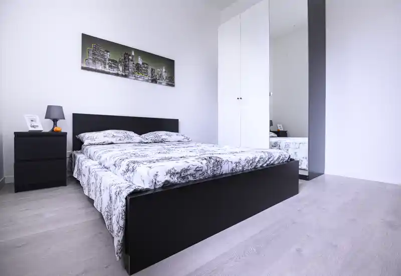 Modern, bright bedroom with a large double bed, bedside table and wardrobe with mirror — clean minimalist styling and soft natural light.