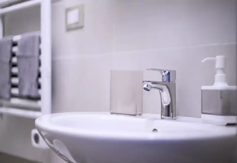 Bright, modern bathroom sink with chrome faucet, soap dispenser and towel rail in soft neutral tones.