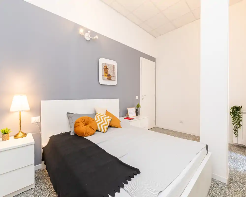 Camera da letto moderna e luminosa con struttura letto bianca, cuscini decorativi e lampada da comodino calda — ben allestita e adatta a foto immobiliari.