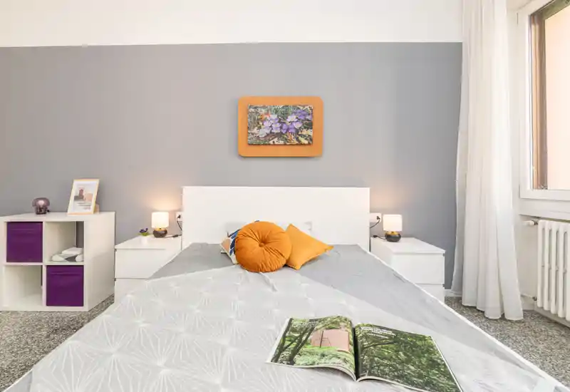 Camera da letto luminosa e ben arredata con letto matrimoniale al centro, cuscini decorativi, comodini e luce naturale dalla finestra.