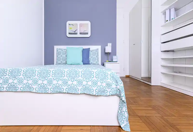 Bright, stylish bedroom with a patterned turquoise bedspread, headboard with accent cushions, bedside table and built-in shelving — a clean, modern sleeping space ideal for rental photos.