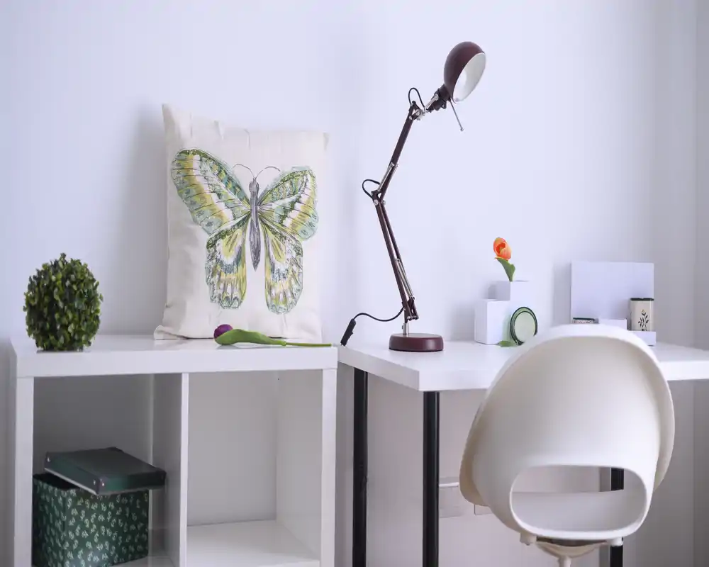Zona de escritorio luminosa y minimalista con silla moderna, lámpara ajustable y detalles decorativos — ideal para una pequeña oficina en casa.