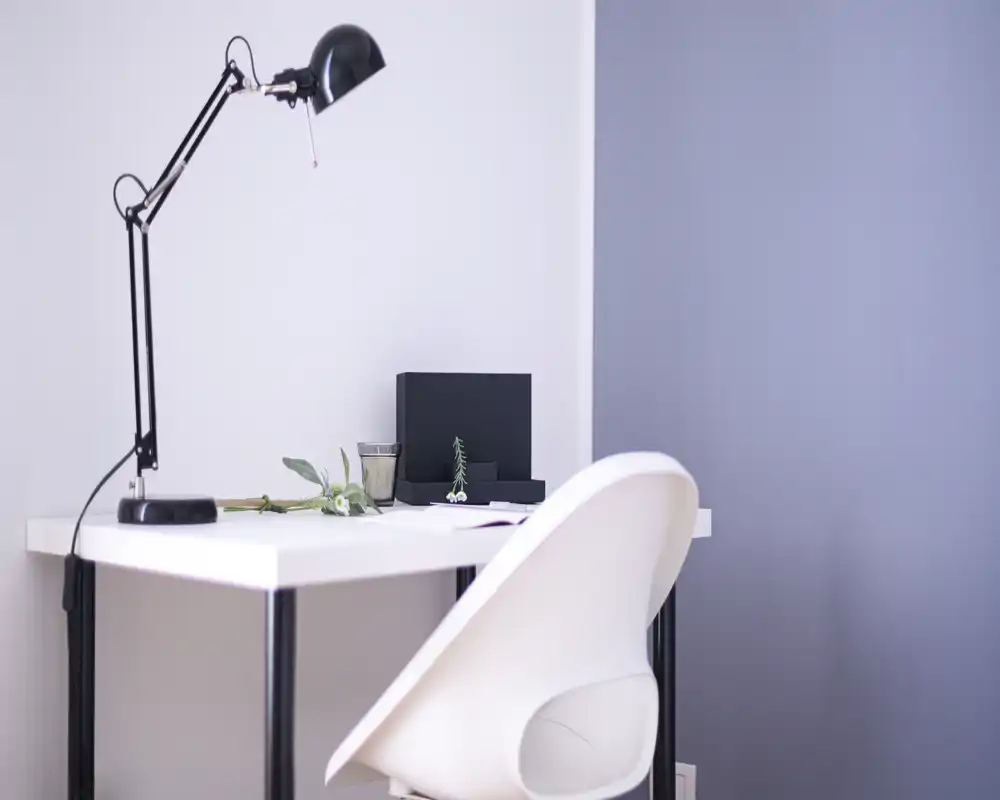 Minimal, bright living area corner with a white desk, modern lamp and chair; clean, Scandinavian-style workspace integrated into the room.