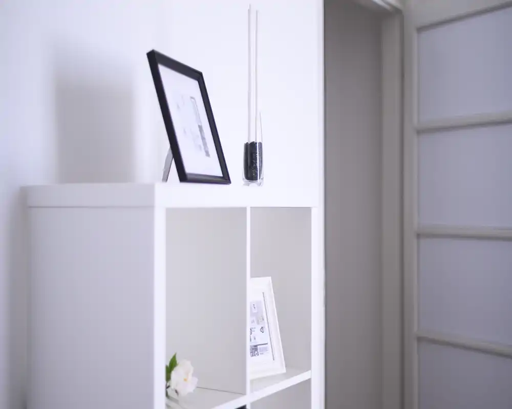 Minimalist white shelving with framed photos and a decorative vase; bright, clean accent suitable for a living area or hallway.
