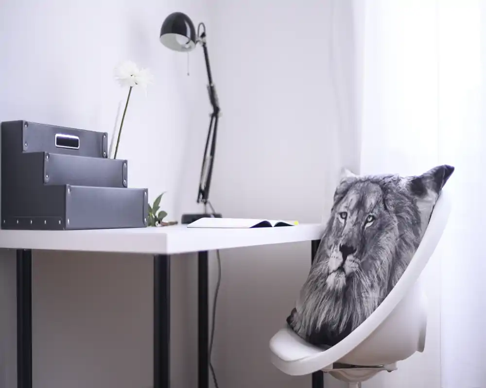 Rincón de trabajo luminoso y minimalista con escritorio blanco, lámpara ajustable y cojín decorativo con estampado de león en la silla — elegante y despejado, ideal para concentrarse.