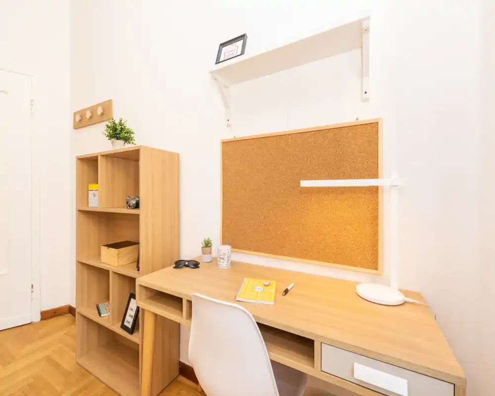 Angolo studio luminoso e ordinato con scrivania in legno, bacheca in sughero, lampada da tavolo e scaffalatura — ideale per lavoro o studio.