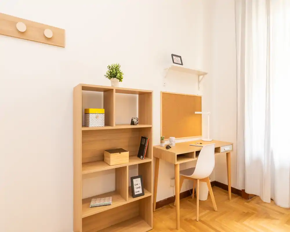 Angolo luminoso e minimalista soggiorno/studio con scaffalatura in legno e una scrivania vicino alla finestra, ideale per lavorare o leggere.