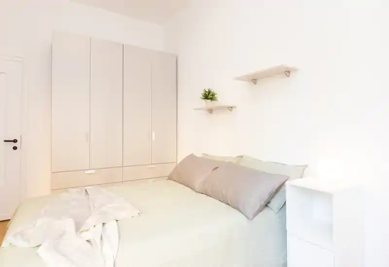 Dormitorio luminoso y minimalista con cama doble, ropa de cama suave, estanterías y armario — ideal para una estancia tranquila.
