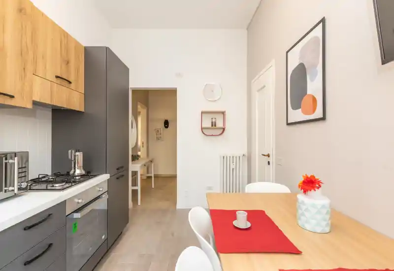Cocina moderna y luminosa con electrodomésticos integrados y pequeña mesa de comedor; mobiliario en madera y gris de líneas limpias.