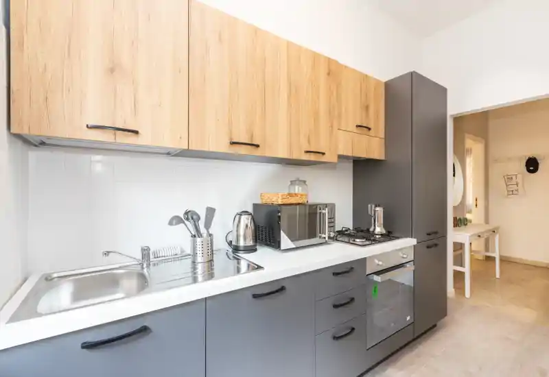 Cocina moderna equipada con muebles bajos grises, armarios superiores efecto madera, fregadero de acero, placa de gas y horno empotrado; luminosa, ordenada y atractiva para anuncios.