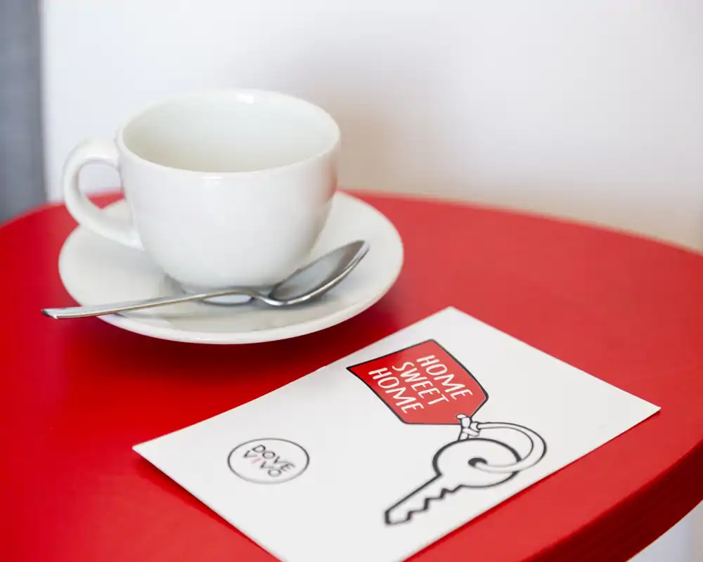 Gros plan d'une tasse blanche avec sous-tasse et cuillère sur une table rouge à côté d'une carte portant la mention « Home Sweet Home ». Photo de détail, pas une vue d'ensemble d'une pièce.