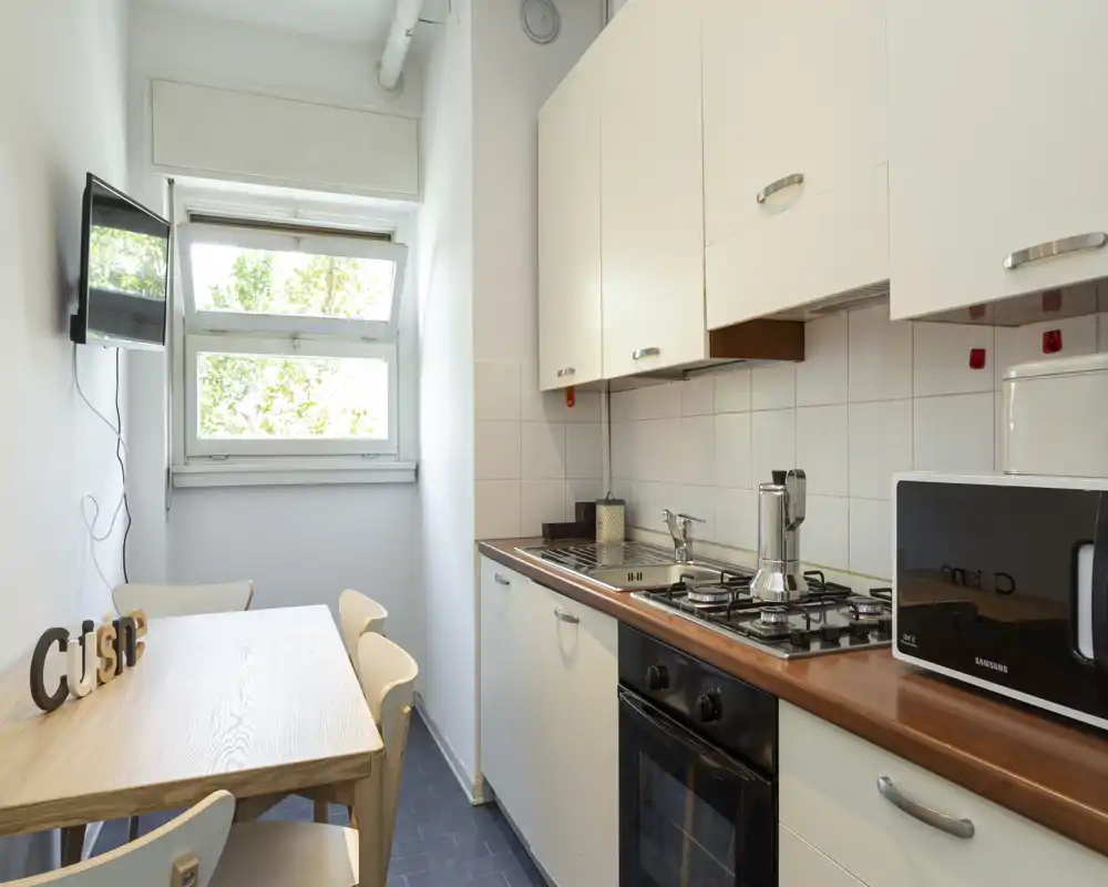 Cuisine compacte et lumineuse avec plan de travail en bois, plaque à gaz et petite table près de la fenêtre — propre et fonctionnelle.