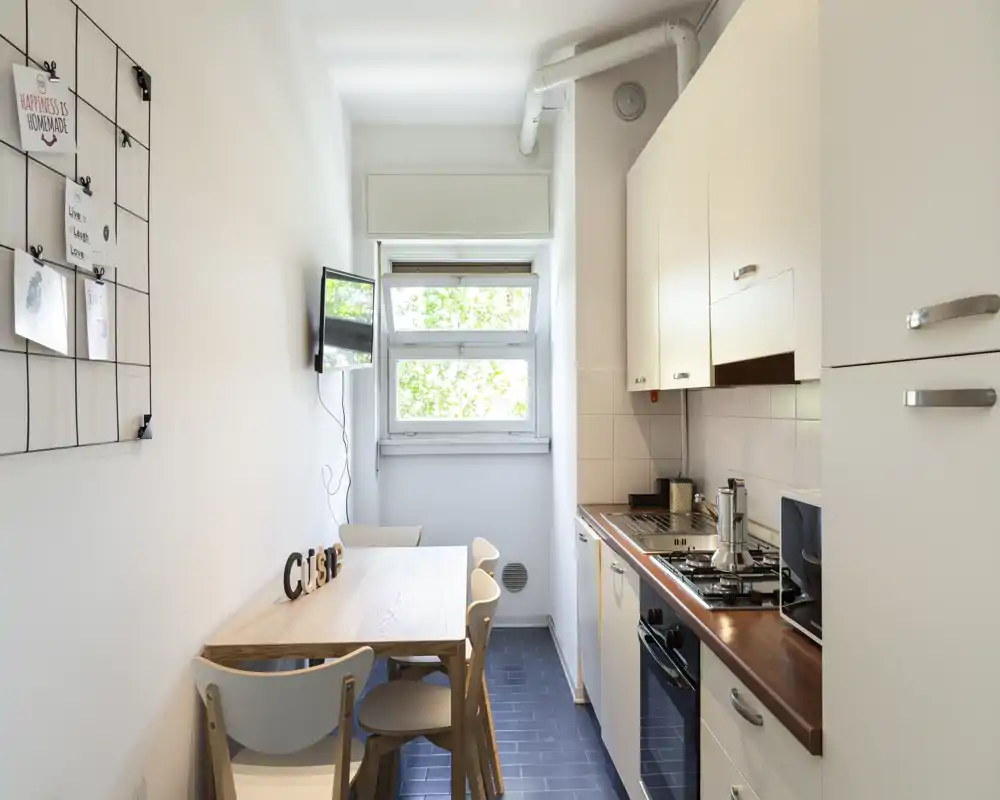 Cuisine étroite et lumineuse avec plan de travail en bois et petite table pour quatre personnes ; agencement compact et moderne avec fenêtre apportant la lumière naturelle.