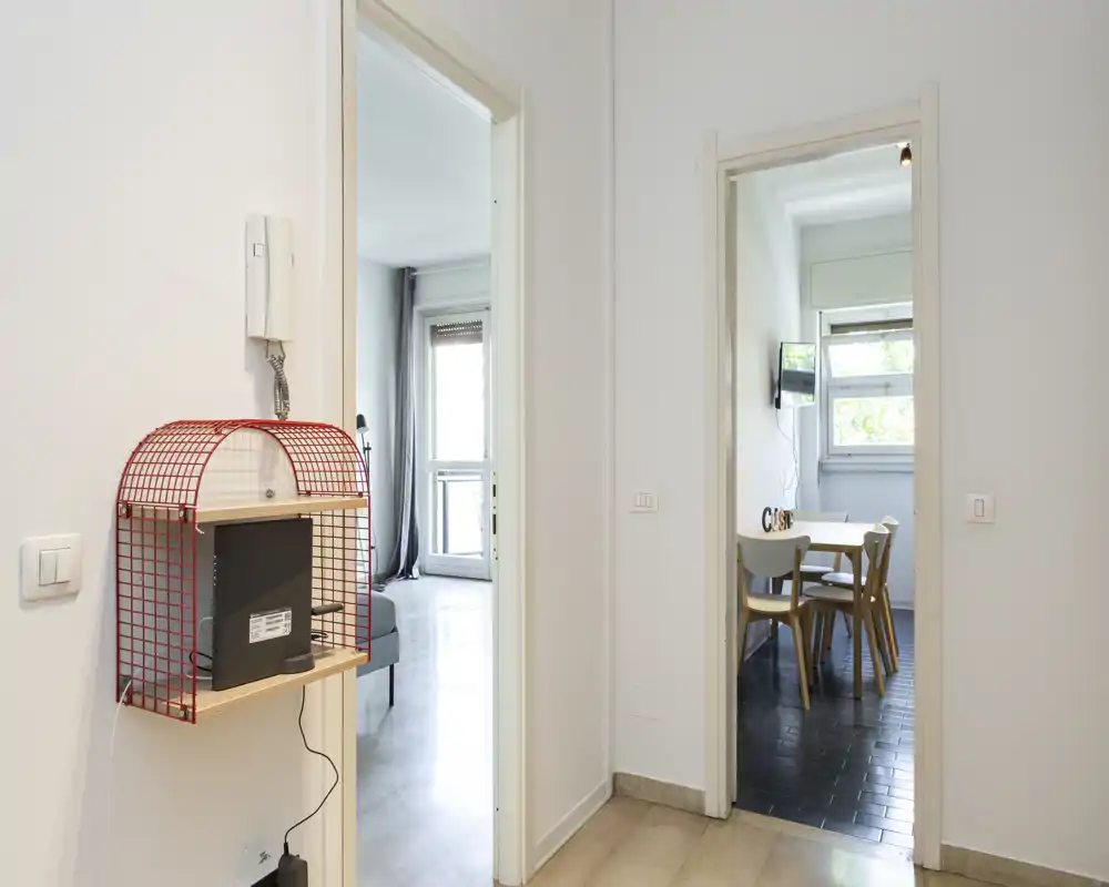 Entrée/hall lumineuse et minimaliste avec une étagère en métal et des portes ouvrant sur le salon et la salle à manger ; murs neutres et lumière naturelle pour une bonne première impression.