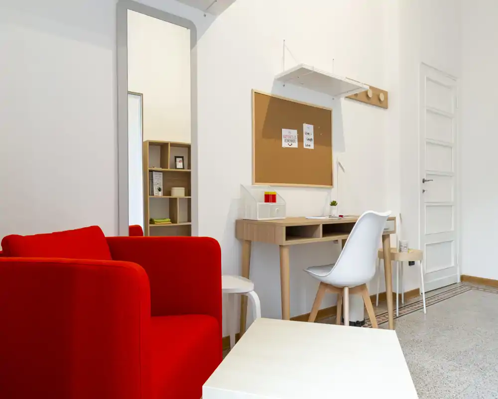Bright, modern living area with a bold red armchair, compact desk and mirror — a neat, Scandinavian-inspired corner ideal for relaxing or working.
