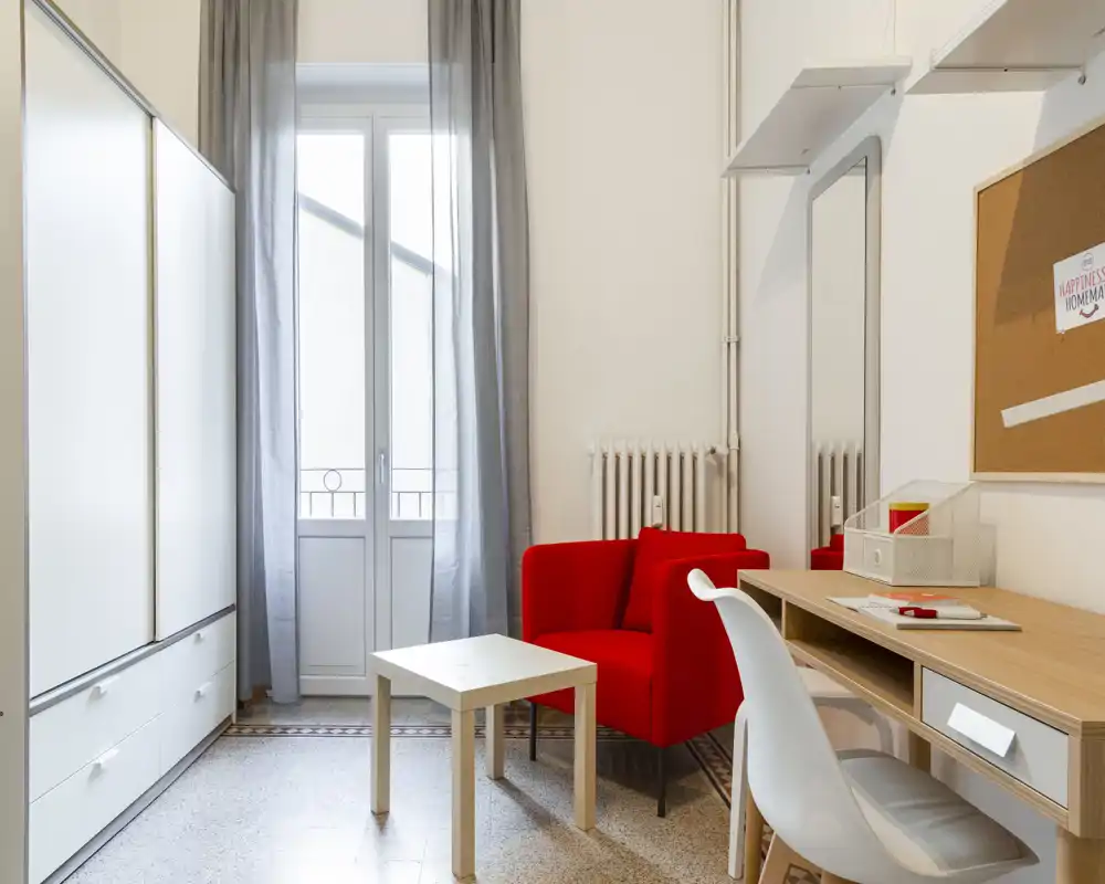 Bright, well-styled living area featuring a bold red armchair, small coffee table and a desk by a tall window that fills the room with natural light.