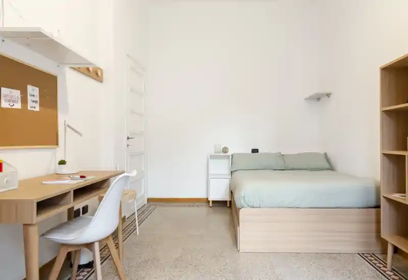 Dormitorio minimalista y luminoso con cama de madera clara, mesita y un escritorio ordenado. La habitación está bien iluminada y presenta una estética nórdica limpia.