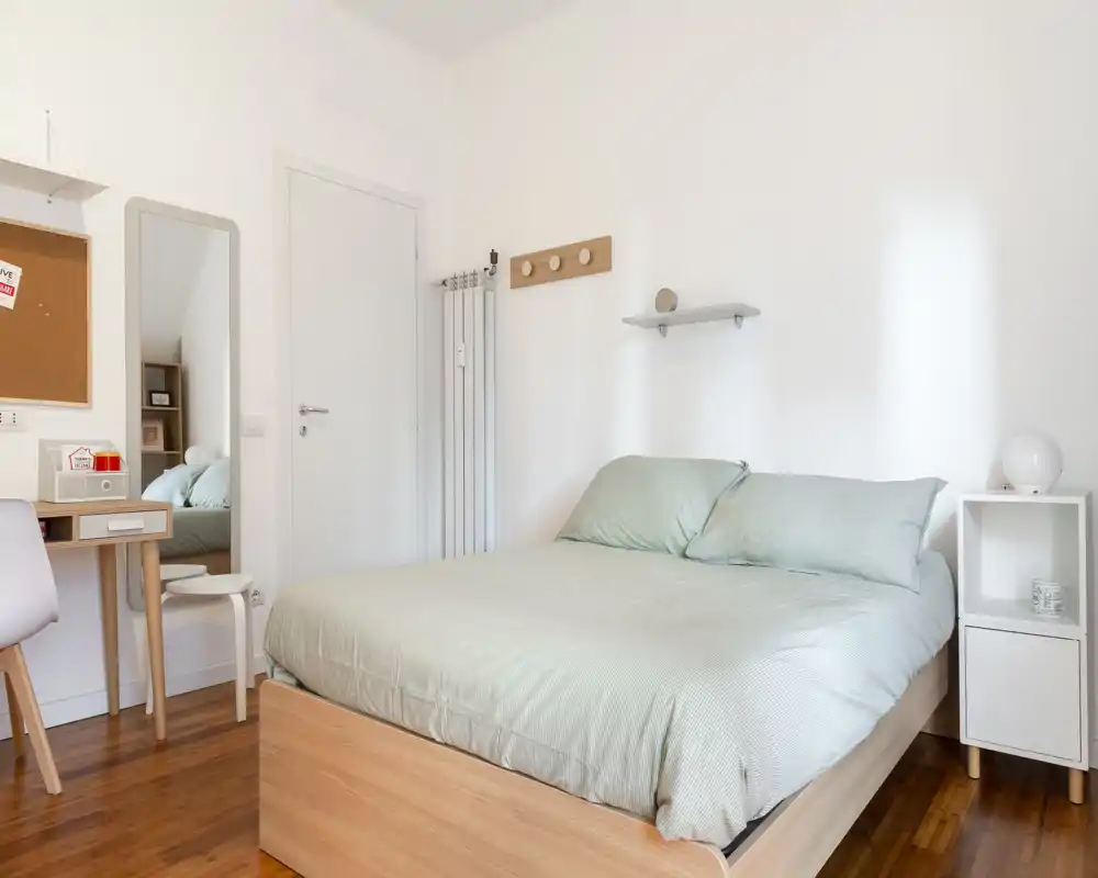 Camera da letto luminosa e moderna con letto matrimoniale in legno e biancheria color menta; luce naturale e arredi minimalisti creano un’atmosfera calma e accogliente.