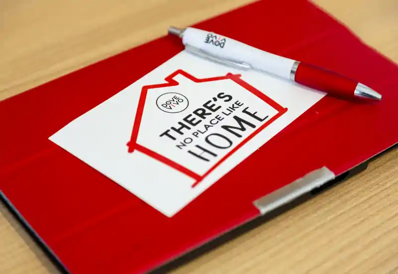 Gros plan d'une housse de tablette rouge avec un stylo et une carte indiquant « There's no place like home » sur une surface en bois — un détail décoratif, pas une photo d'une pièce identifiable.
