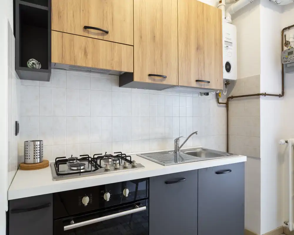 Cuisine moderne et compacte avec plaque à gaz, four encastré, évier en inox et placards effet bois — pratique et bien éclairée pour la vie quotidienne.