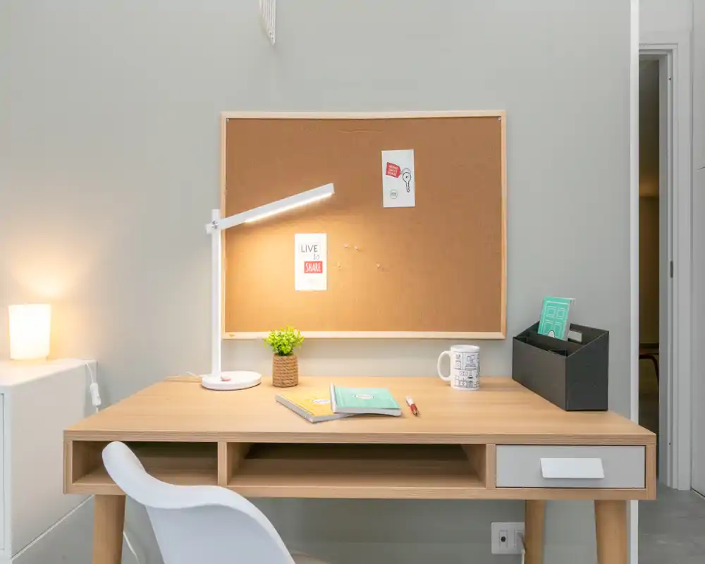 Compact, bright home workspace with a wooden desk, task lamp, cork noticeboard, chair and minimal accessories — ideal for focused study or remote work.