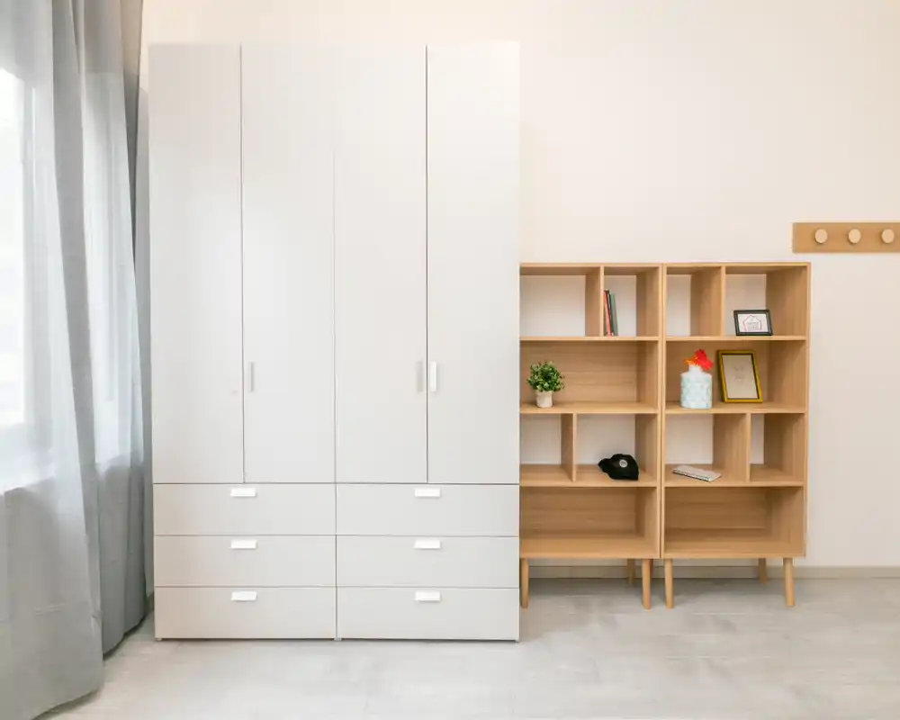 Area di deposito minimal e luminosa della camera da letto con un grande armadio bianco e scaffalature in legno chiaro accanto a una finestra con tende leggere.