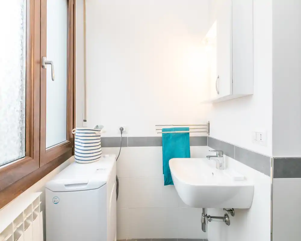 Clean, bright bathroom with a wall-mounted sink, towel rail and a washing machine beside a frosted window.