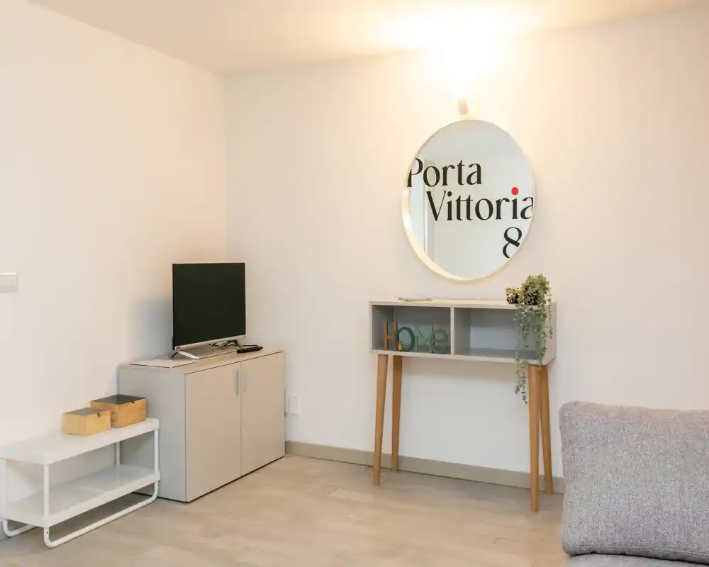 Minimal, well-lit living area with a small TV cabinet, console table with decorative plant and a round mirror — simple, modern styling.